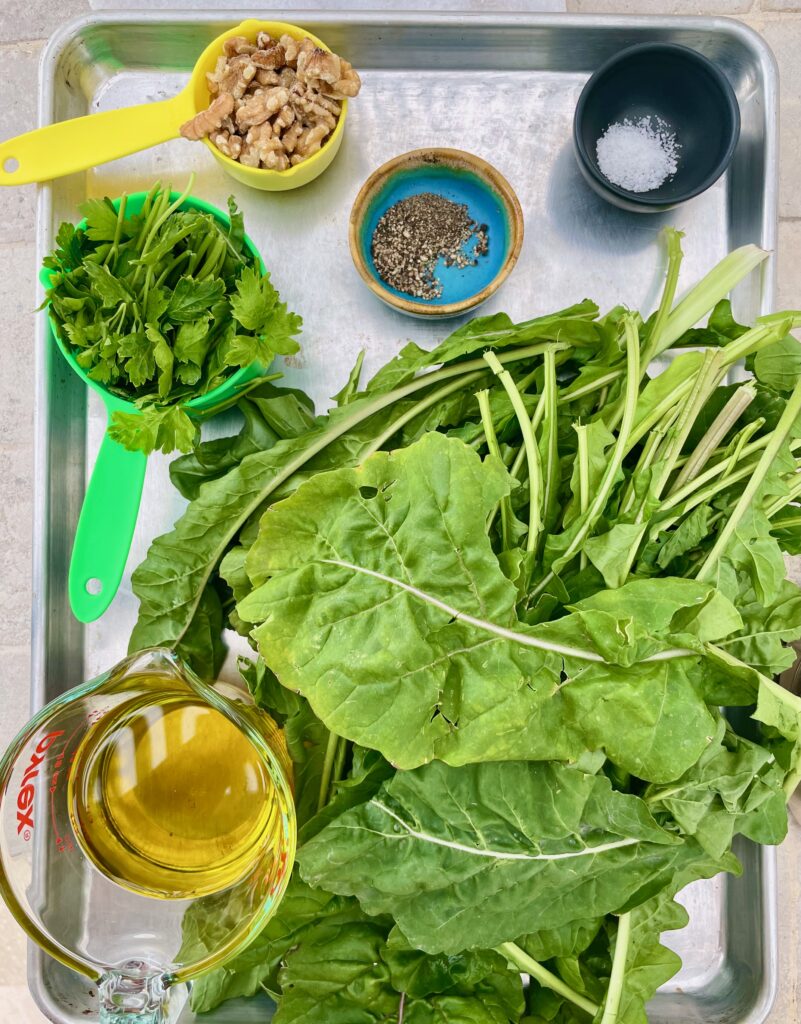 the ingredients for arugula pesto are shown, parsley, walnuts, pepper, salt, arugula, and olive oil