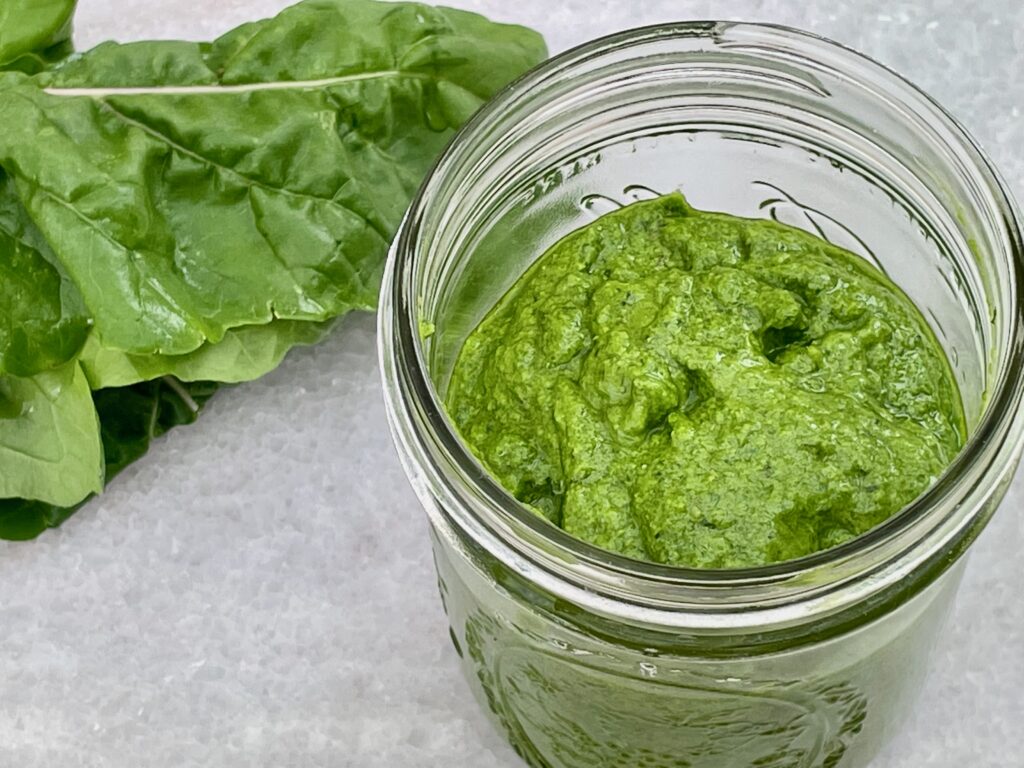 a ball jar of bright green pesto is shown with an arugula leaf in the background