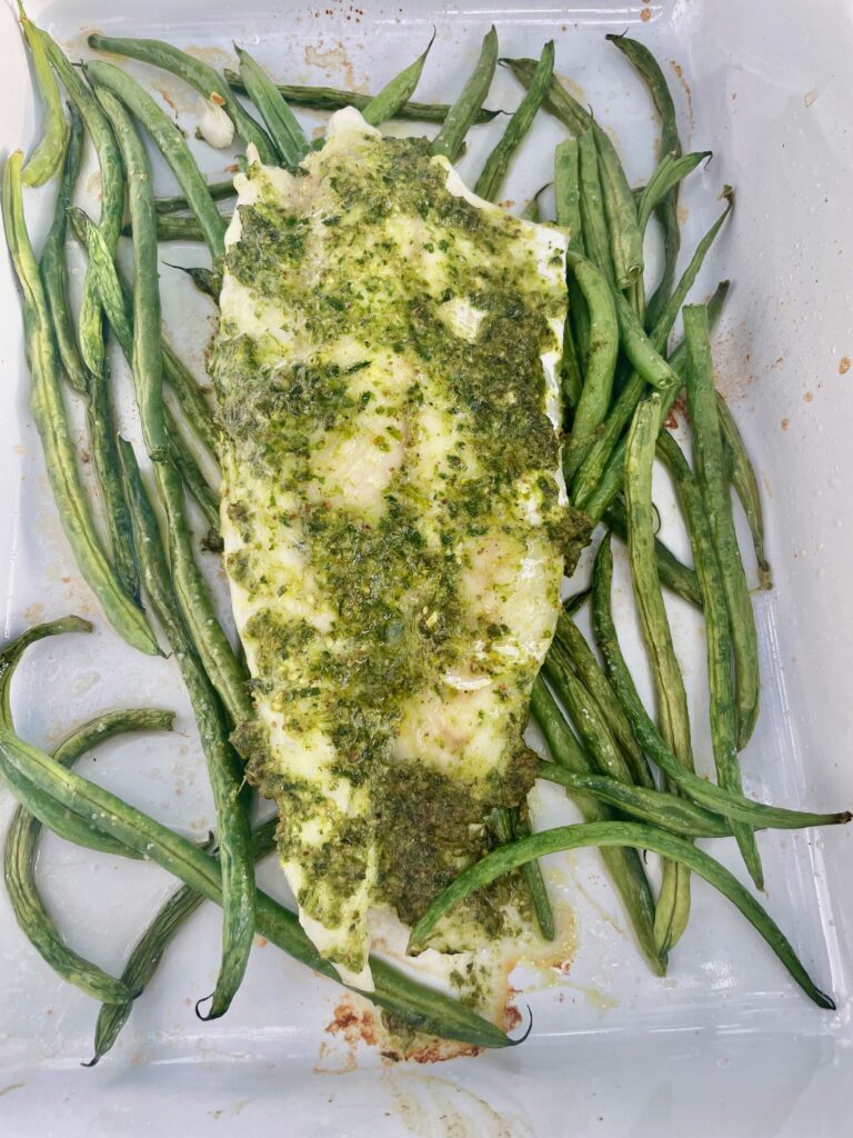 A large filet of sea bass on a bed of string beans. The fish is coated in arugula pesto.
