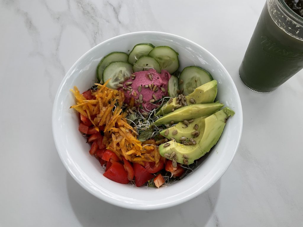 Roast beet dip on top of a salad with rainbow stripes of avocado, cucumber, carrot, and red pepper with the dip in the middle