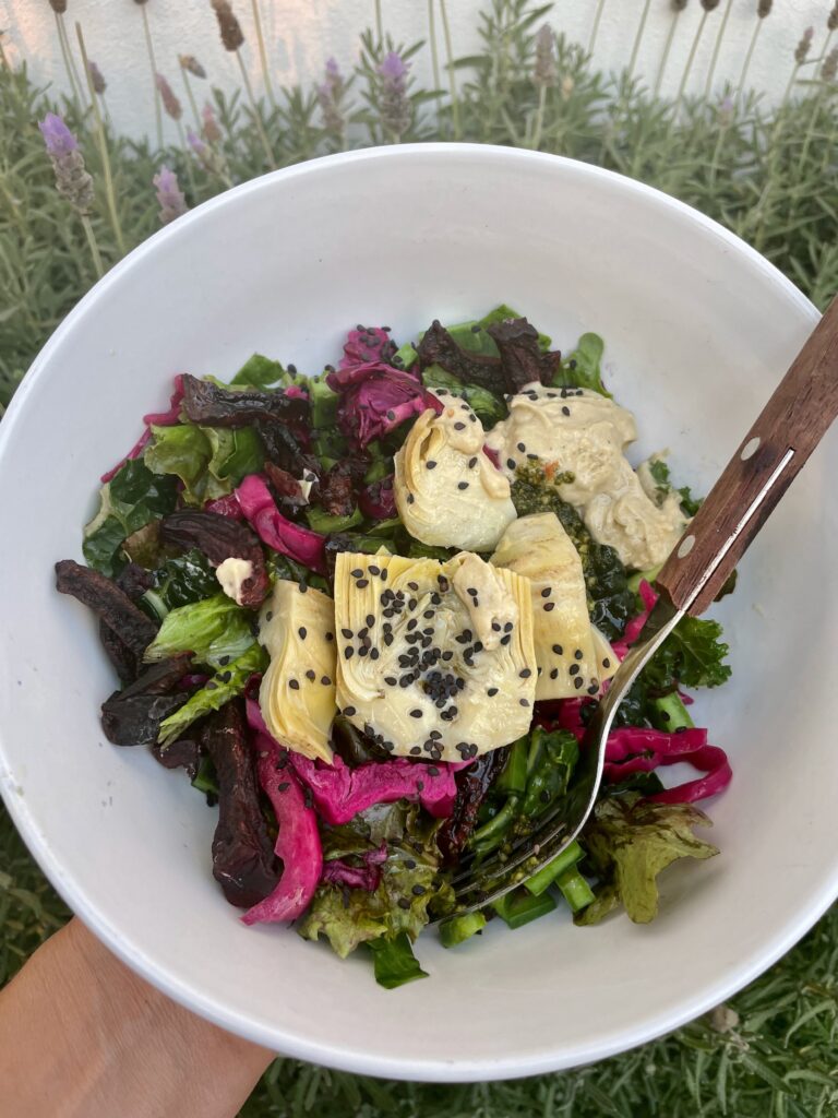 mixed greens are topped with artichoke hearts, red cabbage, and a few sliced fresh green beans are also shown below. 