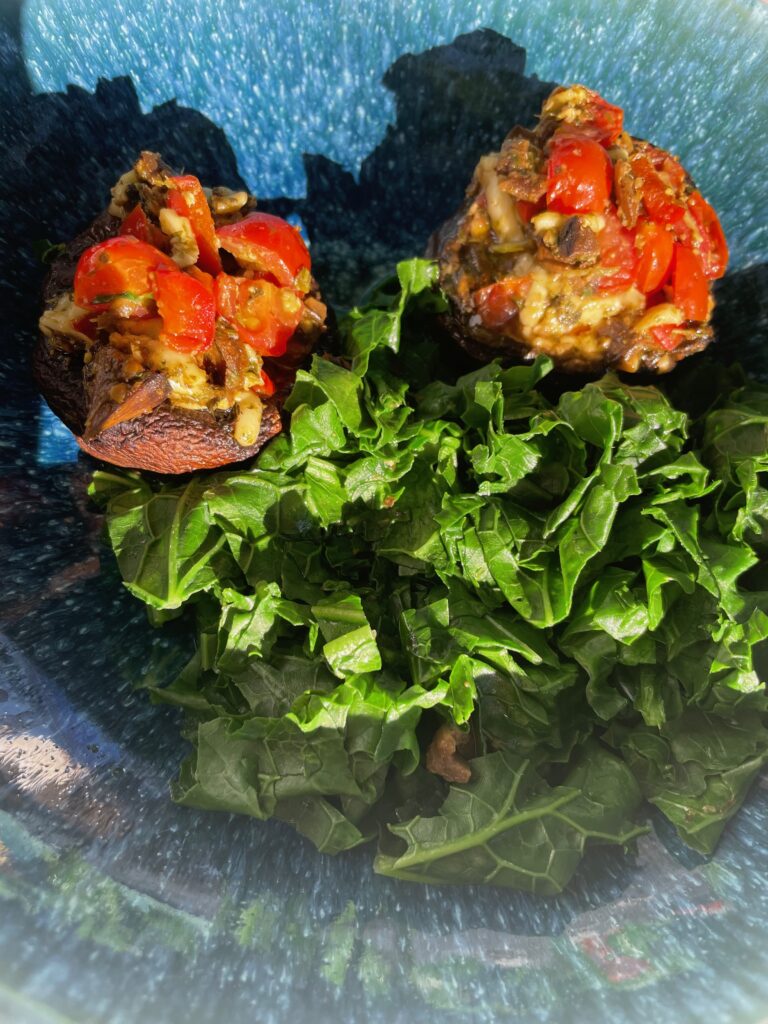 on a blue plate with shadows from the bright sun are mushrooms stuffed with tomatoes tossed in rocket pesto....a side of steamed kale is next tow the two mushrooms