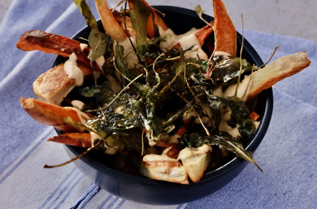 a black pottery bowl is full of sweet potato fries covered with nacho sauce and deep fried greens