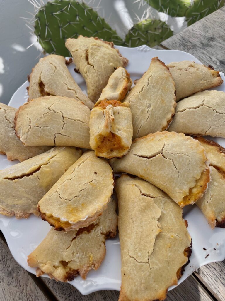 a plate of sweet potato filled empanadas is in front of a cactus leaf in the background