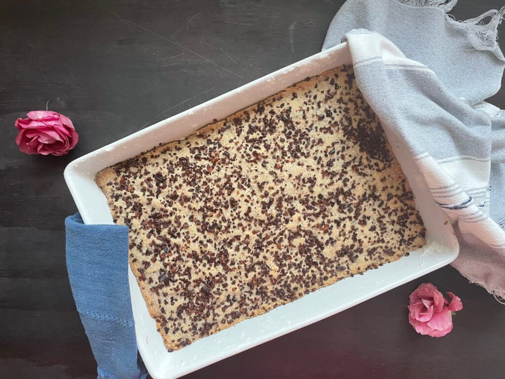 a white crockery pan is full of baked protein cacao bars. a tea towl is on either side, a blue one and a blue and woven striped one. 