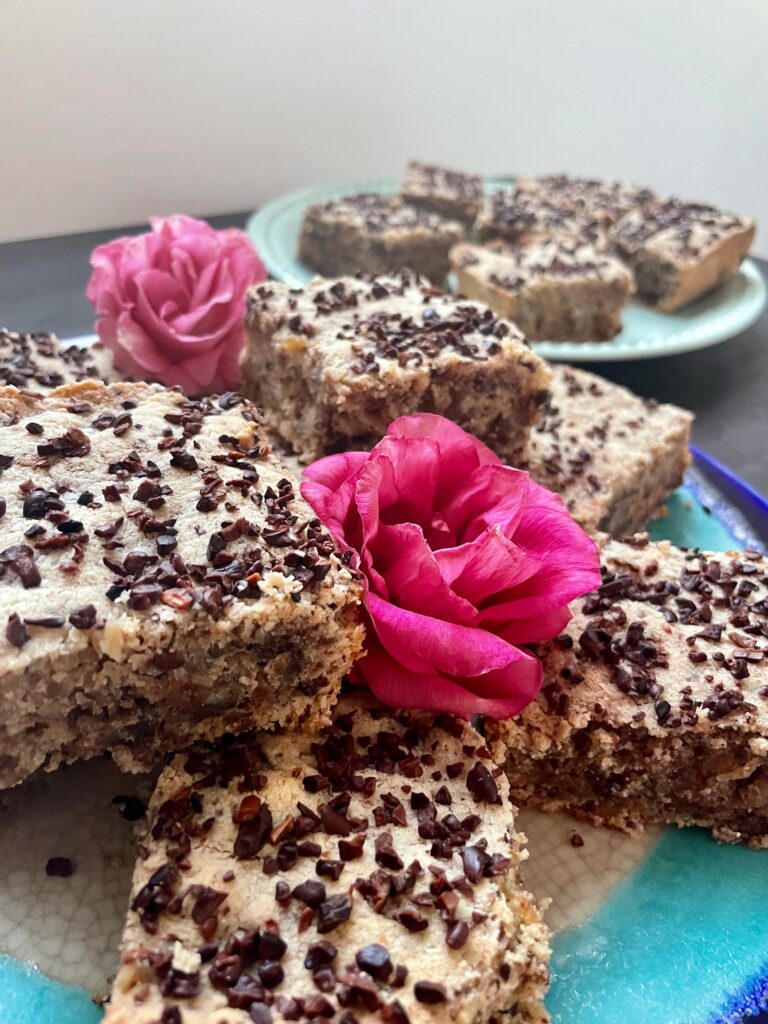 an angular arrangement of square bars sit atop a brilliant blue pottery plate. The cookie bars are mottled wiht cacao chips and two roses that are brilliant pink are nestled in the bars.