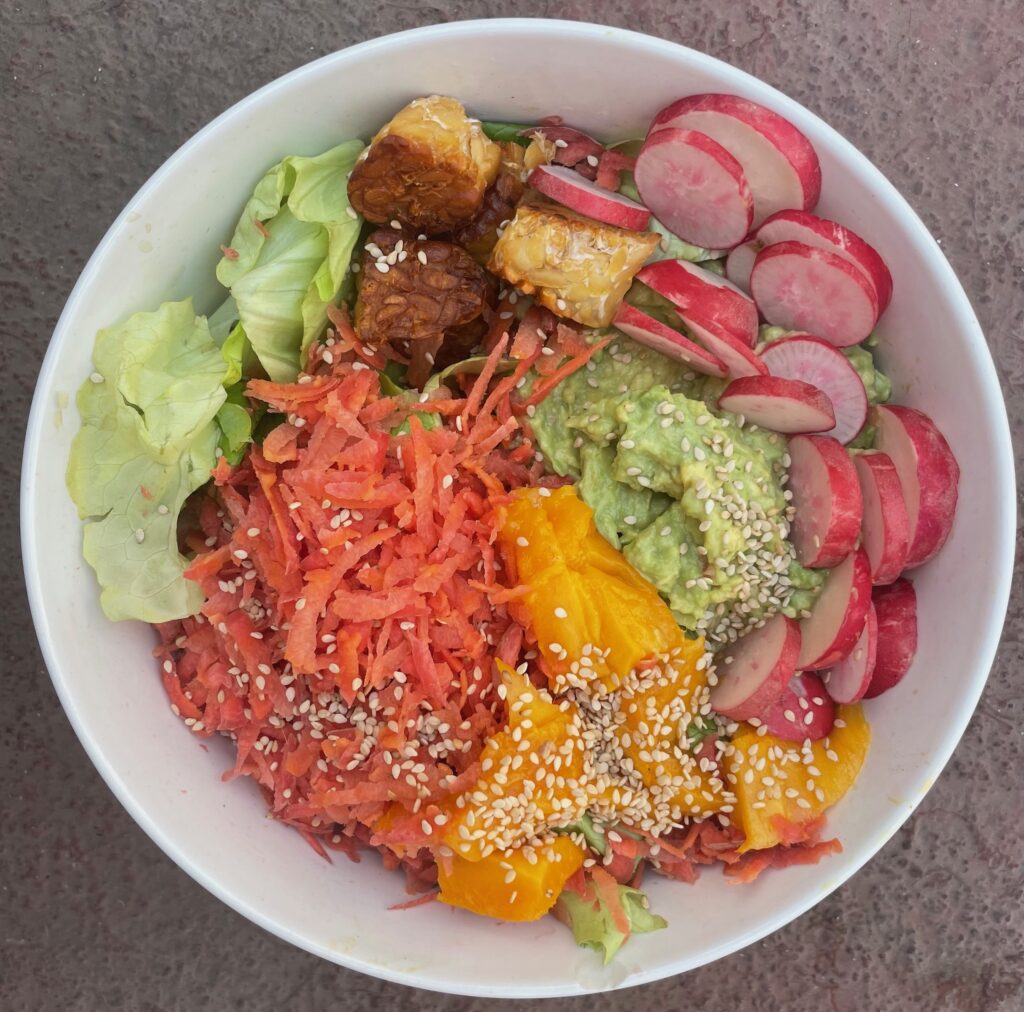 hydroponic lettuce topped with a greated deep pink orange carrot, mango, guacamole, radish and fried tempeh, all in a circle 