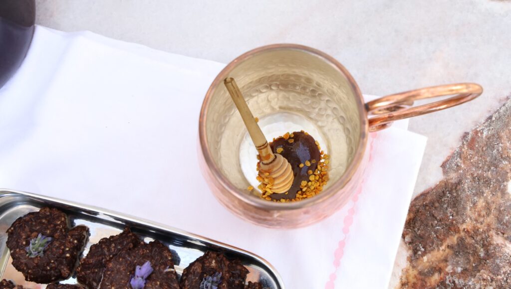 a copper cup is the centerpiece with a bit of dark honey on the bottom of a wooden honey dipping spoon...dripping with honey and a generous sprinkle of bee pollen await tea to be poured into the silver lined mug.