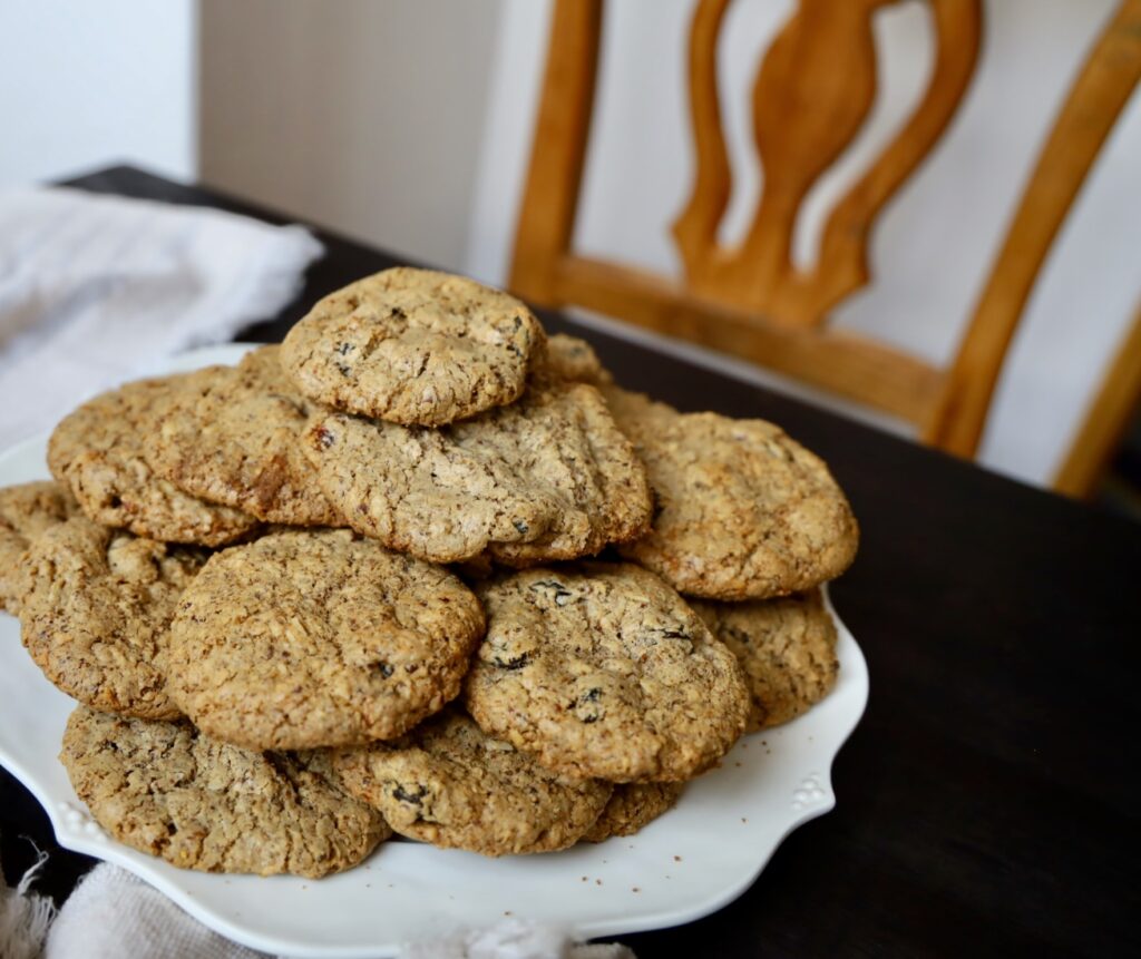 a plate of textured brown cookies are 3 inches across and on a white plate on a dark table with a classic wooden chair in the background.