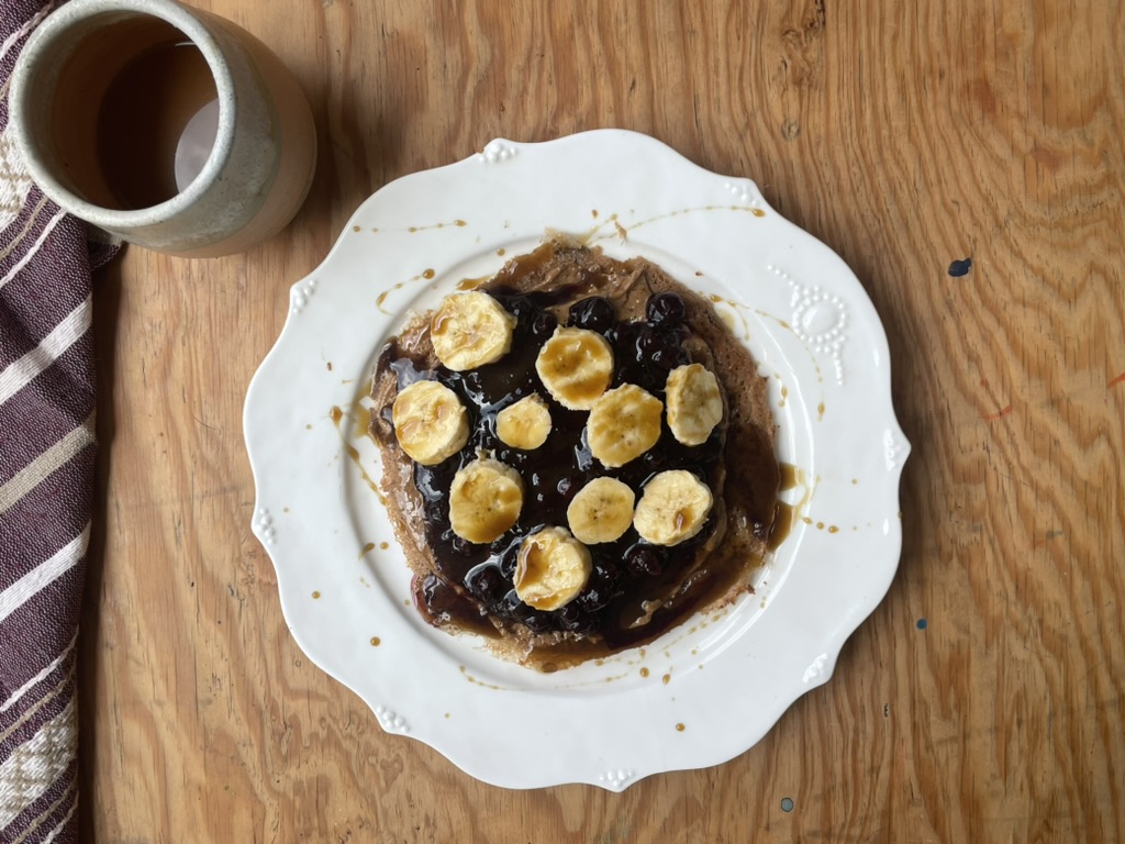 an almond teff wrap, covered in almond butter, blueberry compote, sliced bananas, and covered with blackstrap molasses. and a cup of coffee
