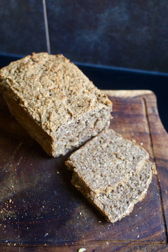 A loaf of chia bread is on a wood cutting board with 2 slices cut out.