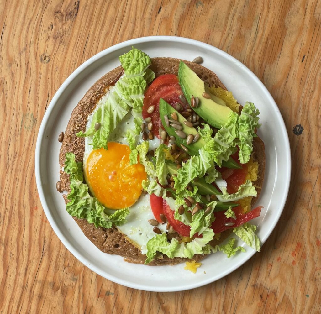 an almond teff wrap is filled with egg, avocado, lettuce, tomato, and sunflower seeds