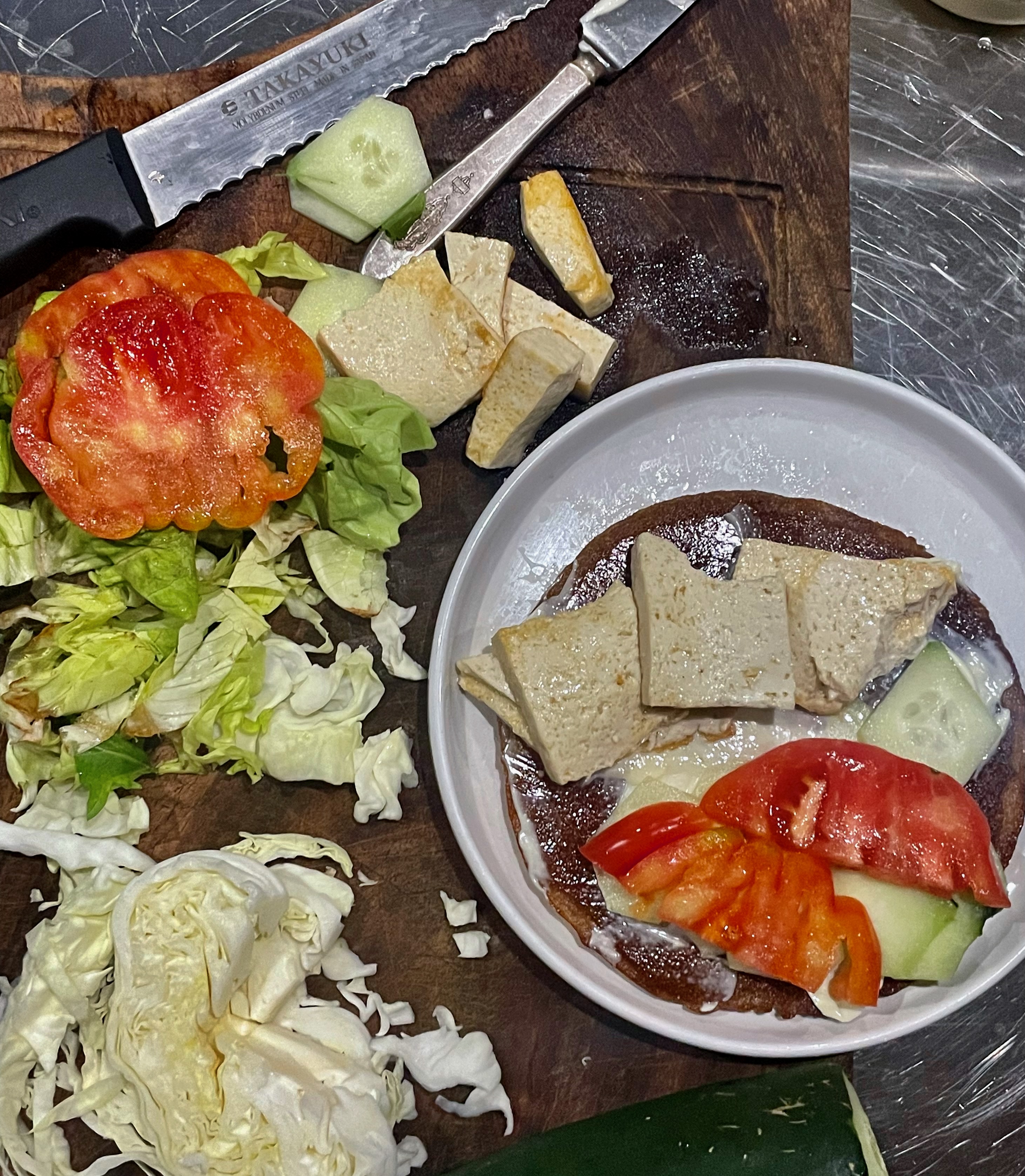 A cutting board is laid out with the ingredients of the crepes: tofu, sliced cabbage, tomatoes, and then a plate with the assembled wrap.