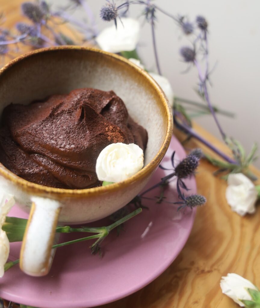 a bowl of chocolate pudding is surrounded by carnations and purple thistles.