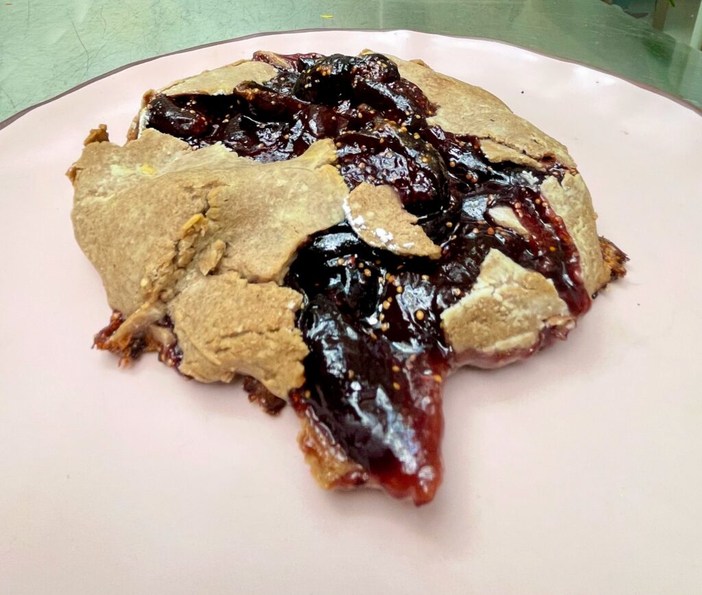 A galette is bursting with fig sauce and on a pale pink plate.