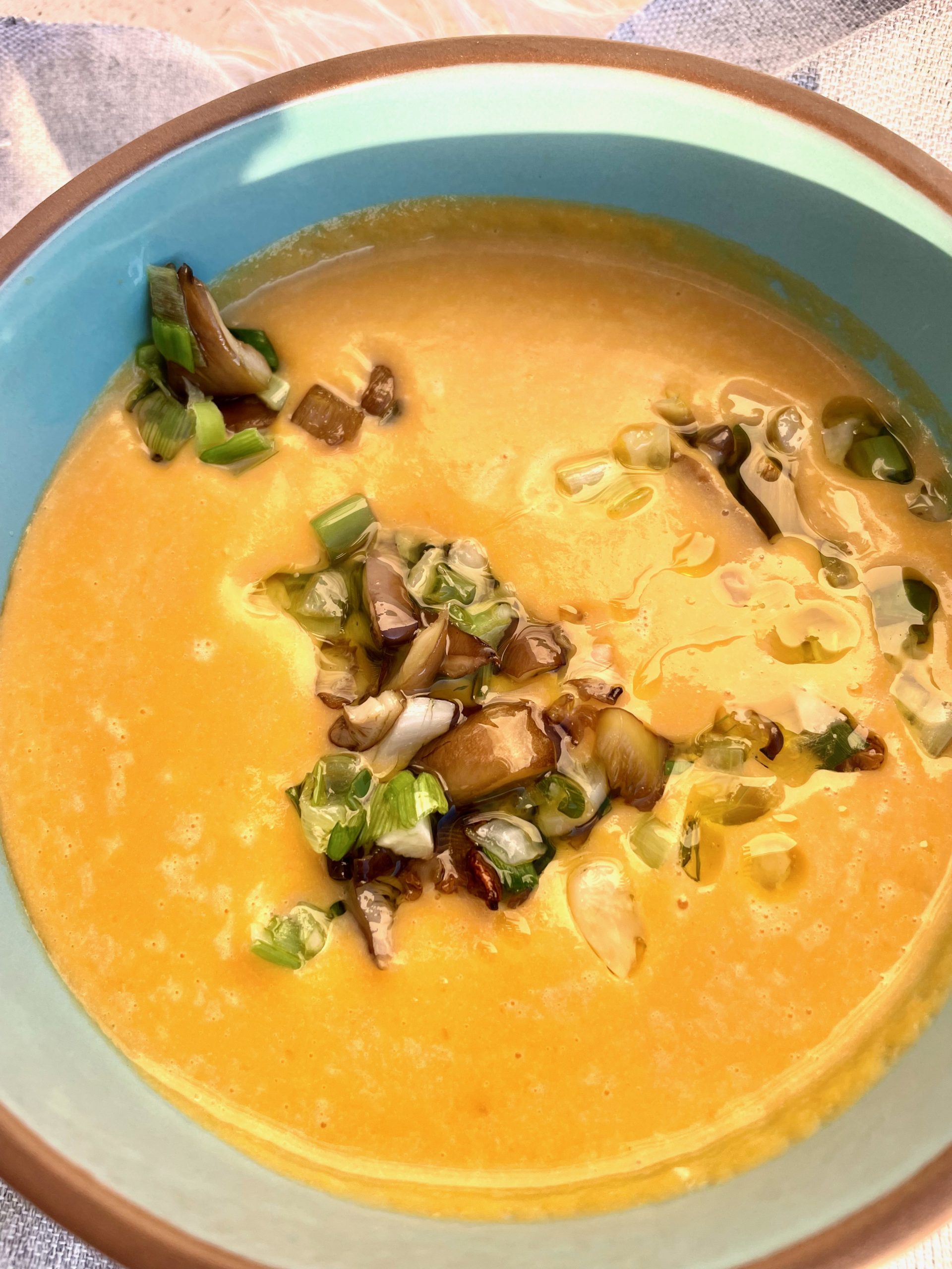 Soup in a blue bowl topped with chopped sauteed oyster mushrooms and green leeks.