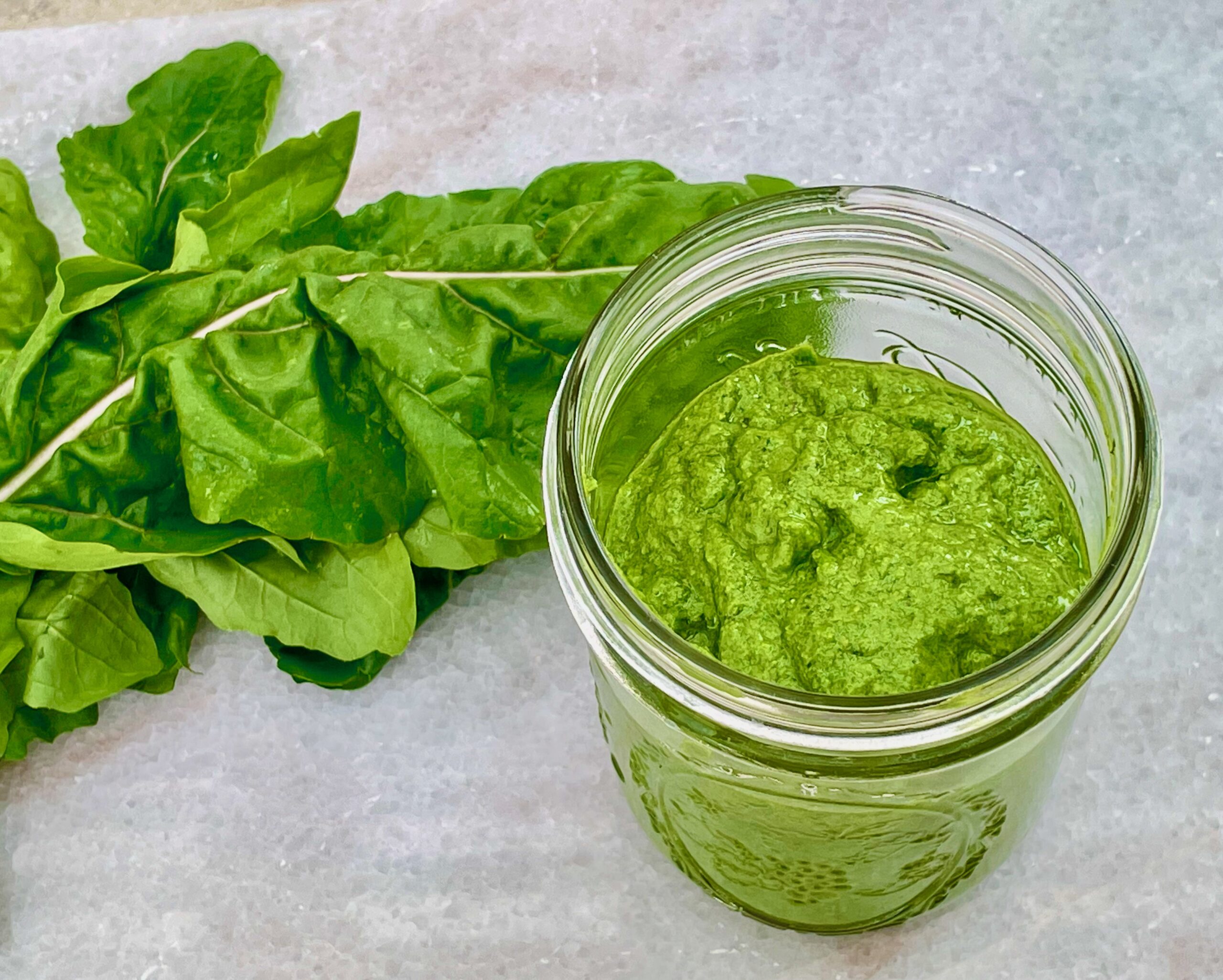 a ball jar of bright green pesto is shown with an arugula leaf in the background