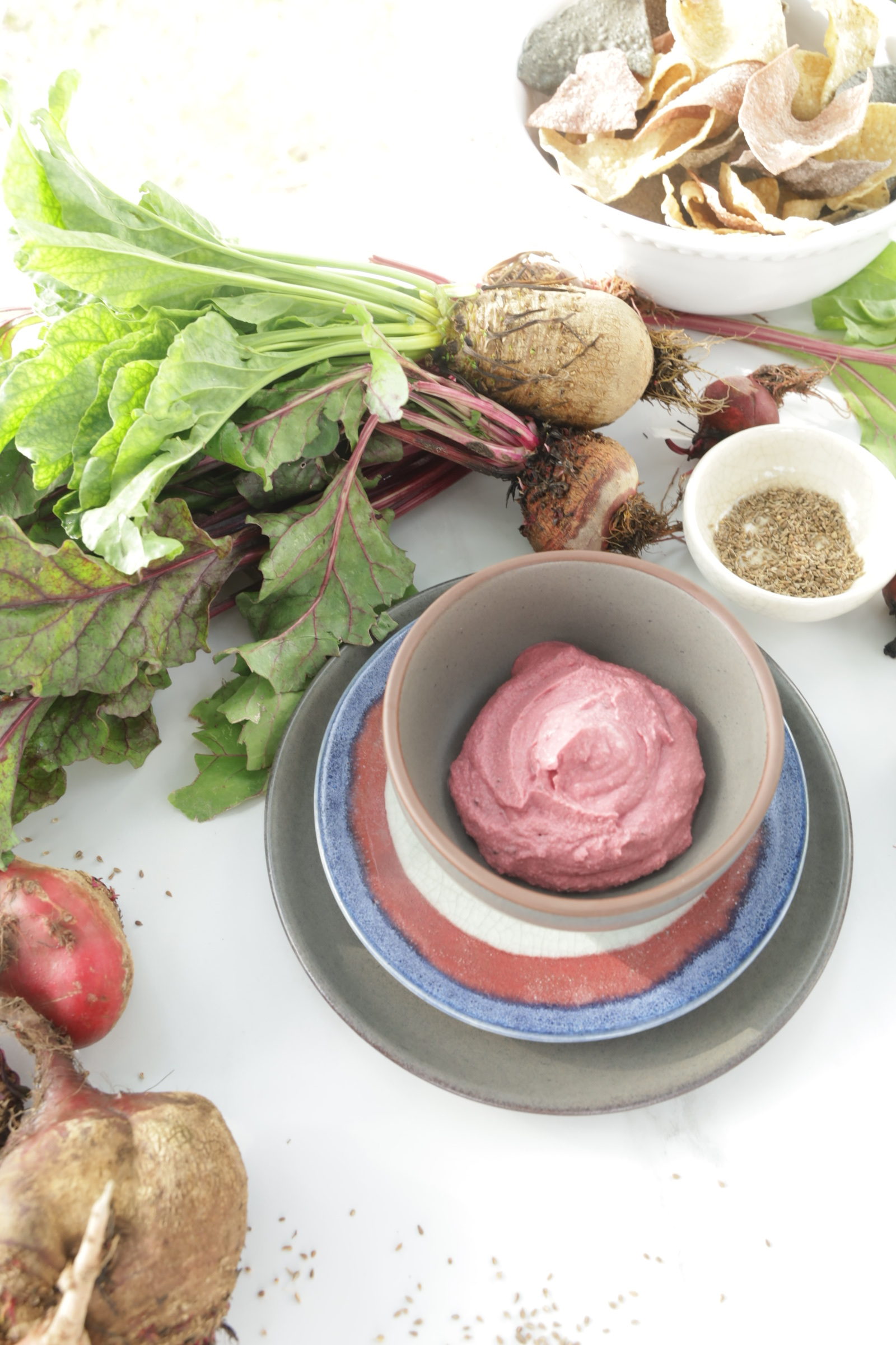 Roasted Beet Root in grey and pink layered pottery surrounded by bunches of beets and sprinkles of anise.