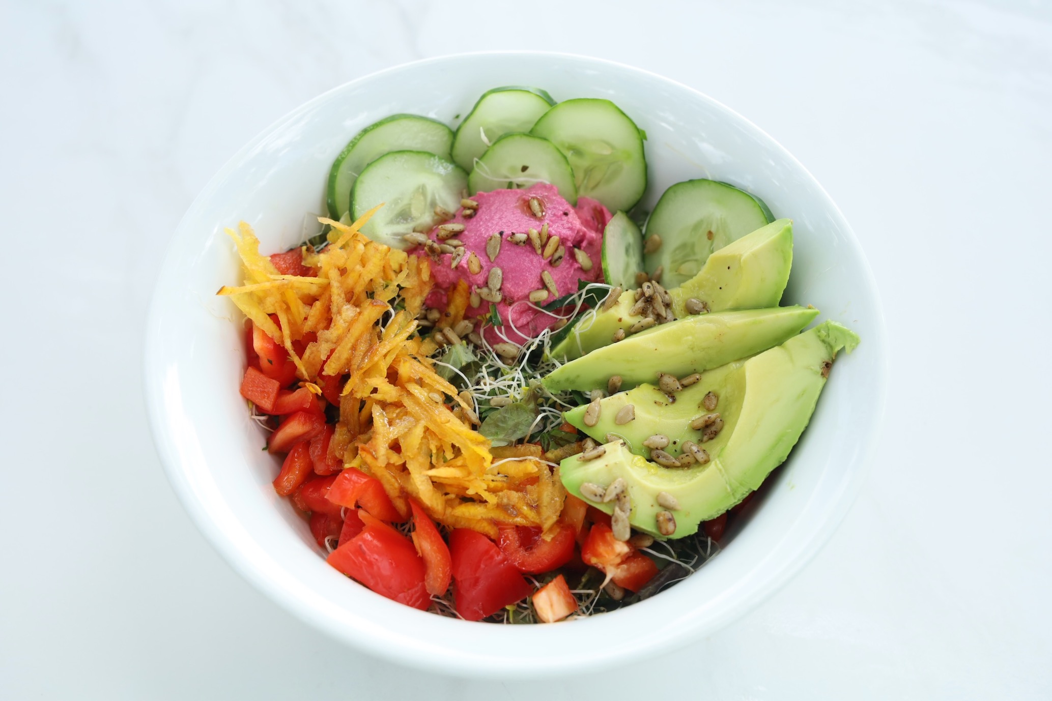 A circular arrangement of food showcases beautiful colors avocado, glimpses of beet hummus, red pepper, cucumber and yellow carrot.