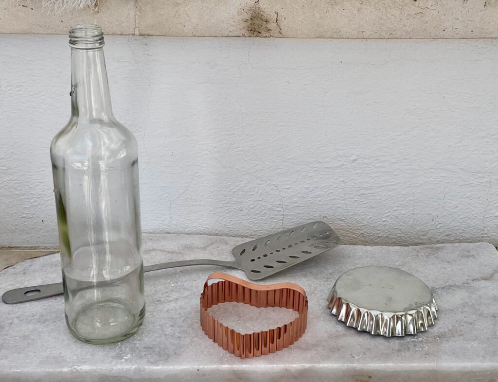 Instruments for making dough, a tall glass bottle, cookie cutters, a metal spatula, and a marble slab.