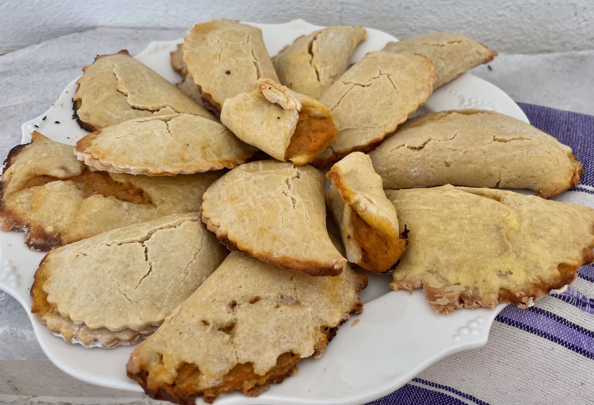 a plate of empanadas, some with bright orange filling spilling out arranged in a concentric circle