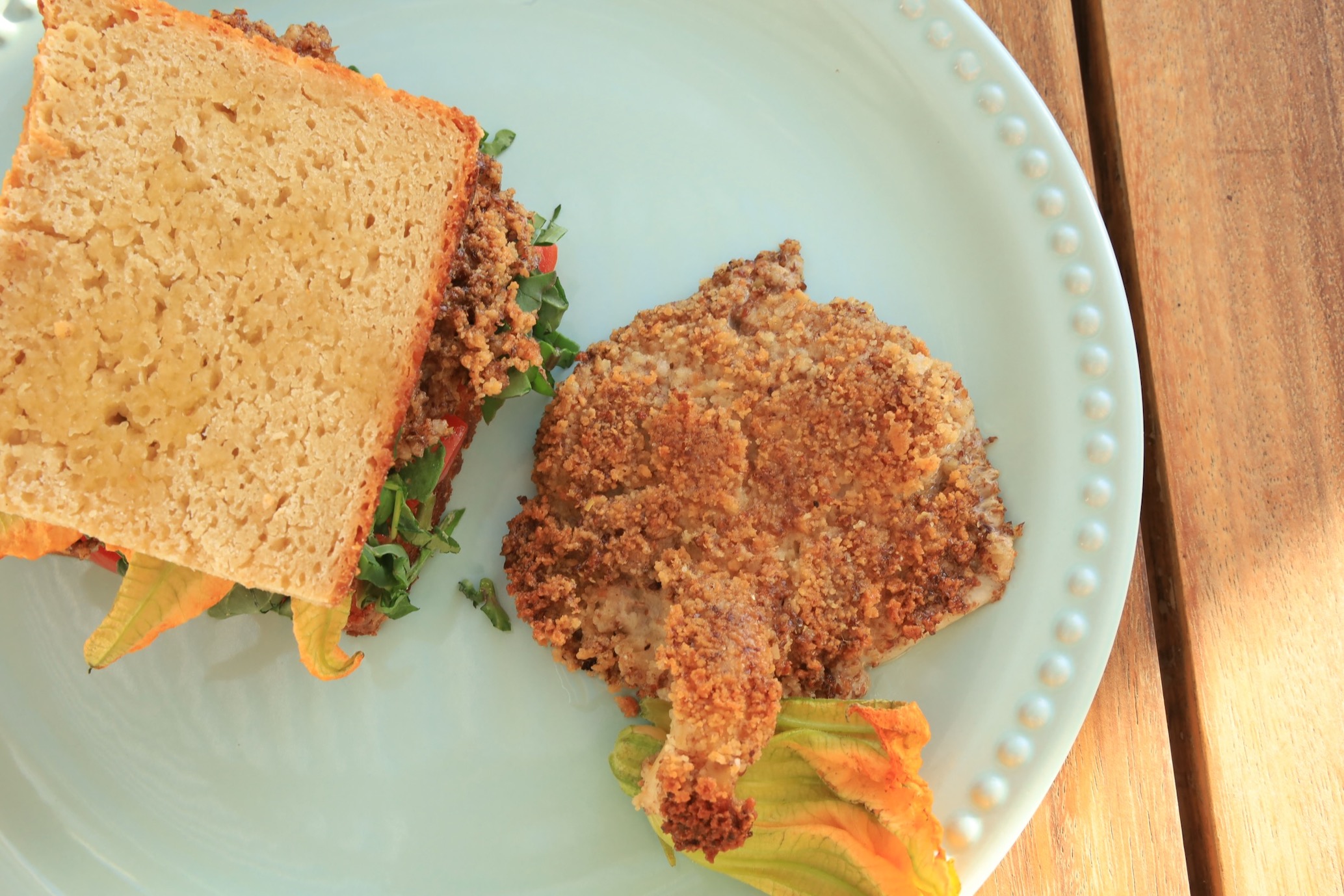 a flat chicken fried mushroom is the center piece on a light turquoise plate with a homemade sandwhich