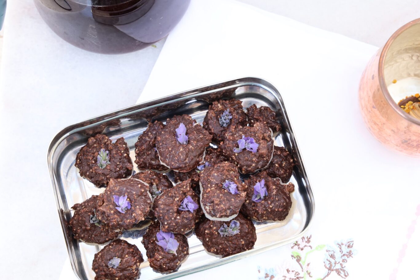 a stainles steel rectangular box hold around 21 mounds of chocolate truffles each topped with a purple lavender flower.