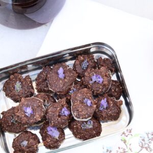 a stainles steel rectangular box hold around 21 mounds of chocolate truffles each topped with a purple lavender flower.