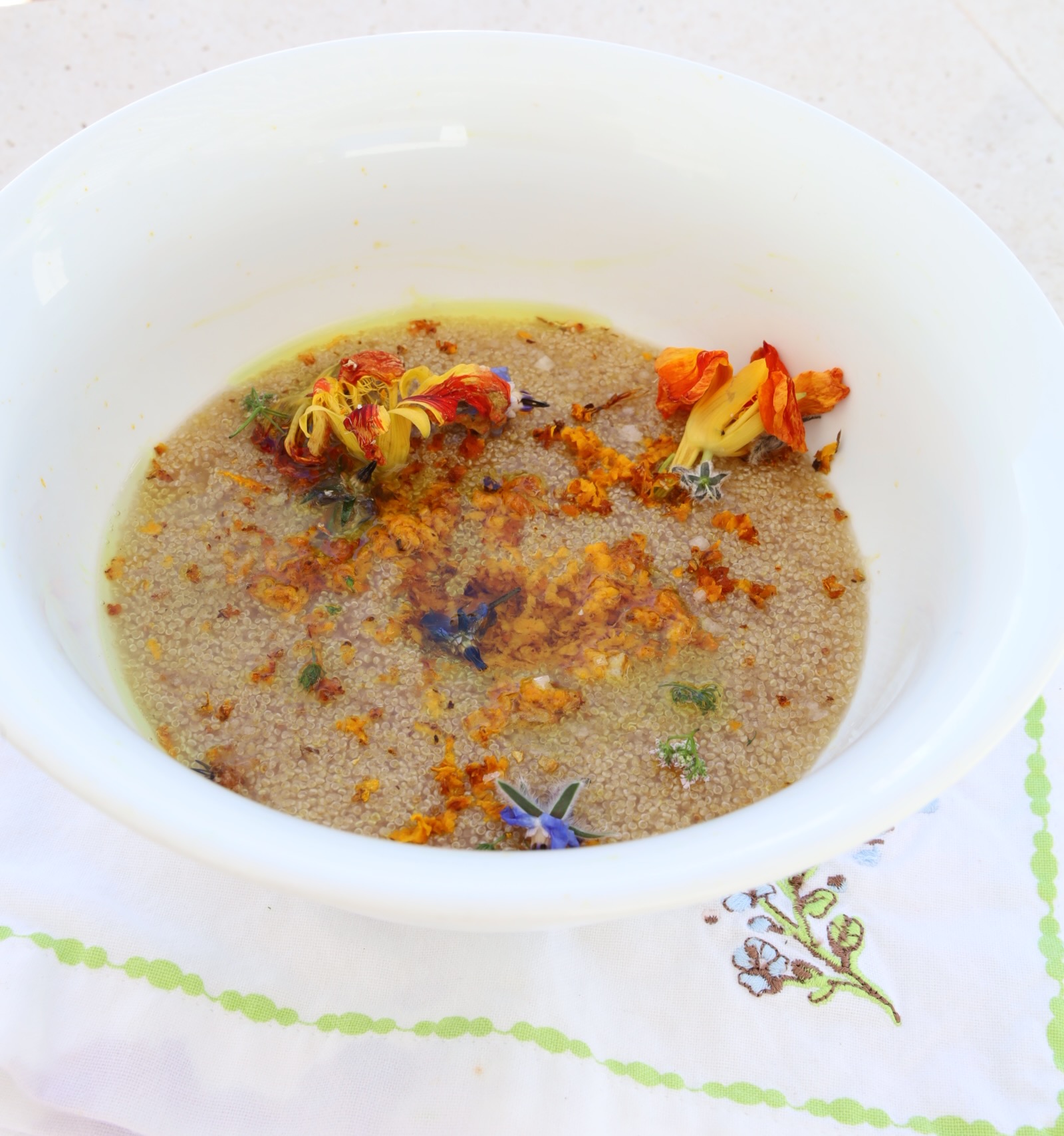 A large sloping white bowl is filled with amaranth porridge and topped with fresh edible flowers, a grate of turmeric and coconut oil that is melted.