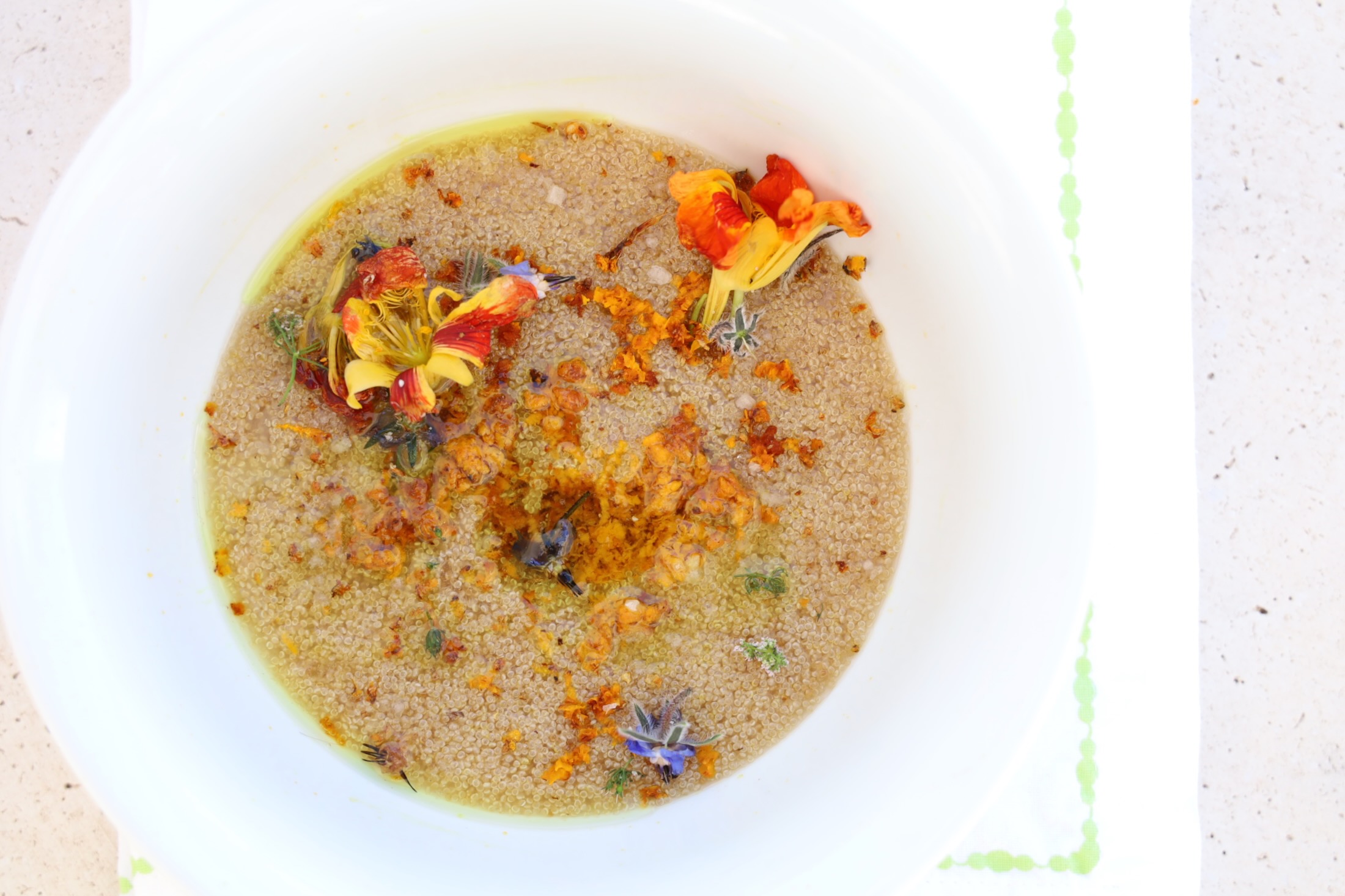 A large sloping white bowl is filled with amaranth porridge and topped with fresh edible flowers, a grate of turmeric and coconut oil that is melted.