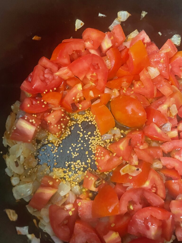 a large cast iron pot holds tomatoes, spices, and onions