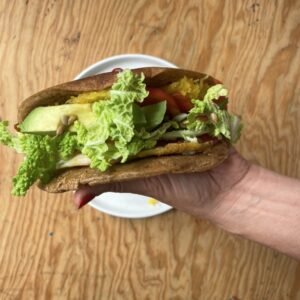 A polished hand holds a wrap filled with egg, avocado, lettuce, tomato, and sunflower seeds