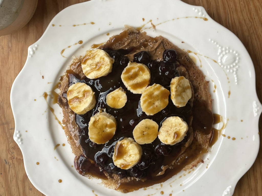 an almond teff wrap, covered in almond butter, blueberry compote, sliced bananas, and covered with blackstrap molasses.