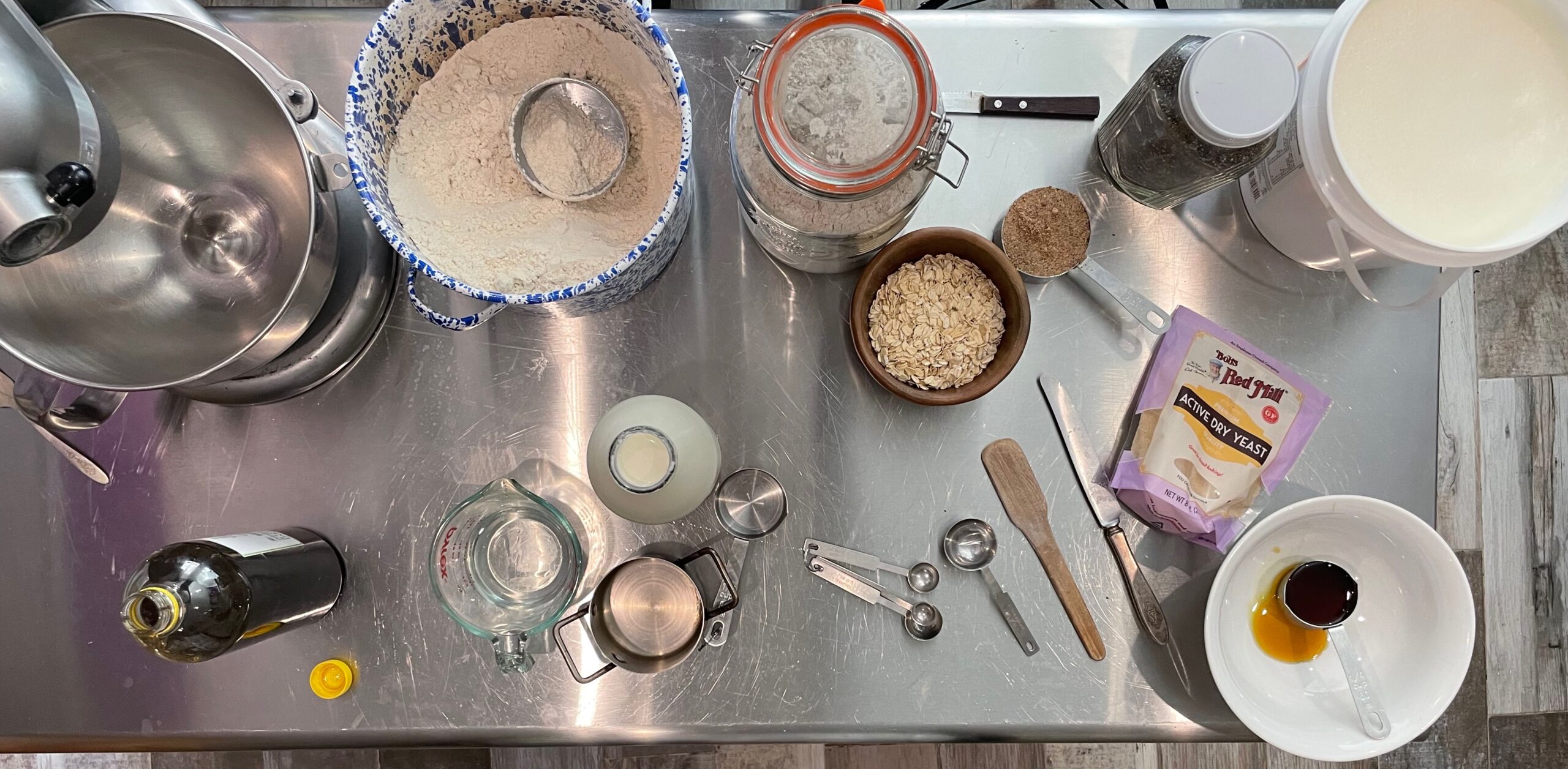 All the ingredients for making chia bread are shown laid out on a stainless steel table along with the needed utensils and equipment.