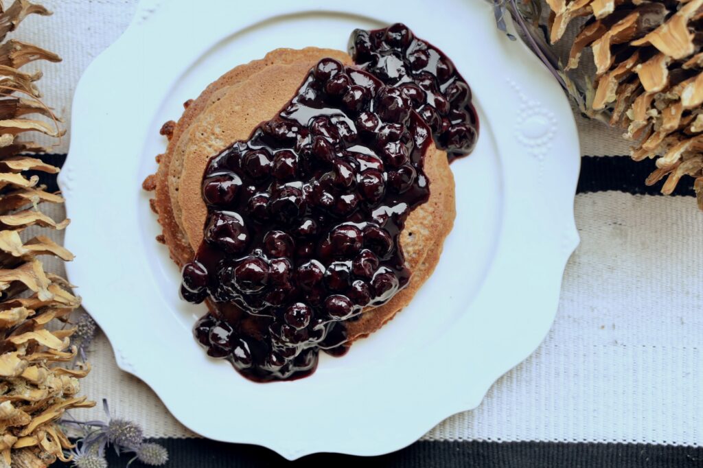 A stack of Blender Pancakes is covered with a large amount of Blueberry Jam Compote on a white plate. The angle is from the top of the pancakes that are on a white plate. 