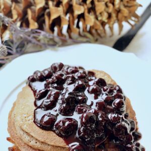 A stack of Blender Pancakes is covered with a large amount of Blueberry Jam Compote on a white plate. The angle is from the top of the pancakes that are on a white plate.