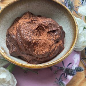 a bowl of sweet potato chocolate pudding is surrounded by carnations and purple thistles.