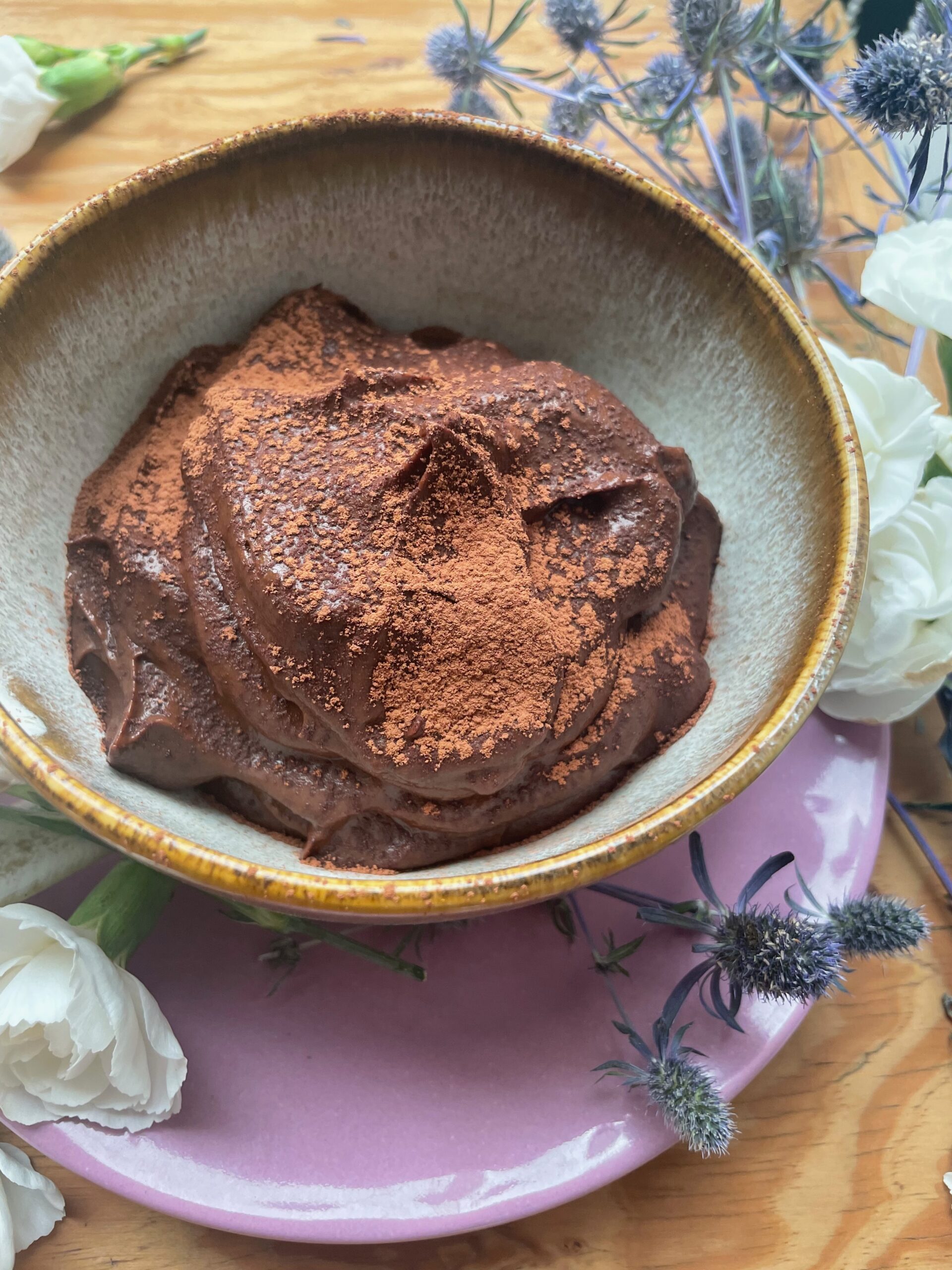 a bowl of chocolate pudding is surrounded by carnations and purple thistles.